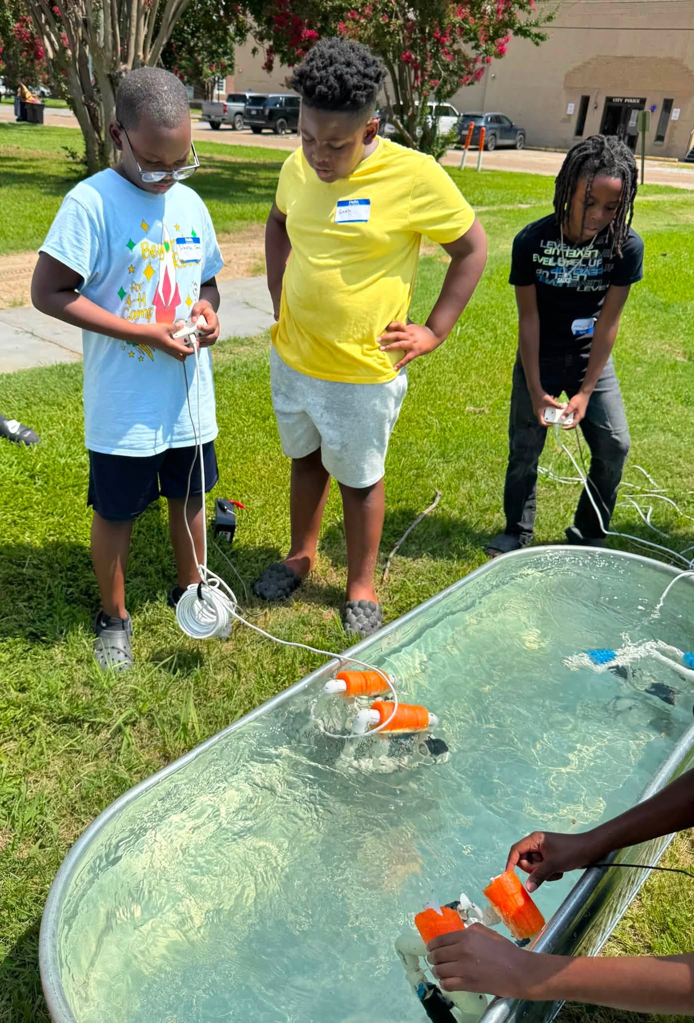 Some kids operating remote controlled flotation devices in a tub of water outside.